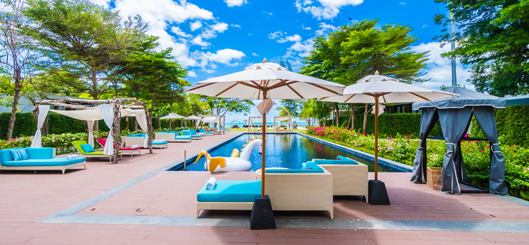 Área externa de pousada com piscina, cadeiras e guarda sol. Uma foto para fazer o marketing para pousadas.